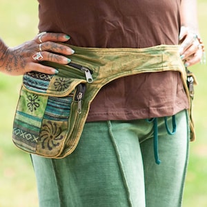 May include: A brown tank top with a green and brown patchwork fanny pack with a zipper. The fanny pack is worn around the waist and has a small pocket on the front.