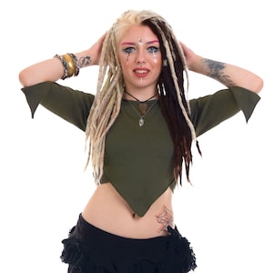 Può includere: Top verde oliva con maniche svasate e orlo unico, abbinato a pantaloni neri e dettaglio in vita con volant. La modella ha dreadlock biondi e marroni e un tatuaggio a ragnatela.