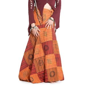 Könnte beinhalten: Ein weinrotes Langarm-Top mit Ausschnitten und Schnürung vorne wird mit einem Patchwork-Maxirock in Orange- und Rottönen kombiniert. Der Rock zeigt verschiedene Sonnen- und Blumenmuster.