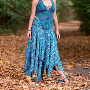 Könnte beinhalten: Eine Frau trägt ein blaues und violettes Batik-Haltertop mit einem blauen und goldenen Blumenmusterrock. Sie steht in einer Waldlandschaft mit heruntergefallenen Blättern auf dem Boden.
