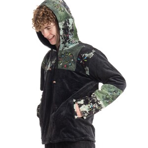 May include: Black hooded jacket with colourful floral and abstract patterns on the hood, sleeves, and upper chest. The jacket has a drawstring closure and pockets. The sleeves and hood are accented with green and black patches.
