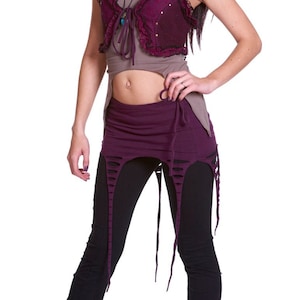 Puede incluir: Una mujer con un chaleco morado y marrón con cuello de volantes, pantalones negros con diseño desgastado y zapatos rosas.