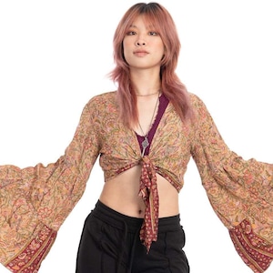 Puede incluir: Conjunto femenino con un top corto de manga larga estampado con mangas acampanadas, atado a la cintura. El top tiene un diseño floral con detalles en rojo y dorado. Combinado con pantalones negros de pernera ancha.