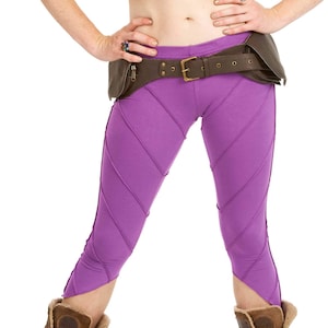 Peut inclure: Leggings violettes avec une ceinture en cuir marron et des bottes en daim marron. Les leggings ont un design unique avec des coutures diagonales.