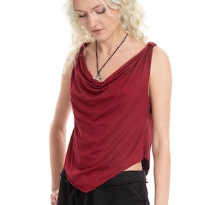 May include: A sleeveless deep red top featuring a draped cowl neckline and knotted shoulder straps. The garment has a pointed hemline that falls at the waist, creating a fluid silhouette. The fabric is a solid, matte material in a dark burgundy hue.