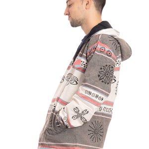 May include: A hooded jacket with a white and gray striped pattern and black and white geometric designs. The jacket has a zipper closure and a drawstring hood.