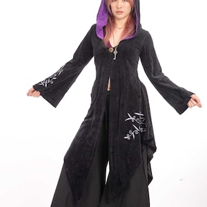 May include: A black long-sleeved hooded coat featuring a vibrant purple inner lining, flared sleeves, and white embroidered vine patterns on the sleeves and hem. The coat has an asymmetrical hemline and a single front closure.