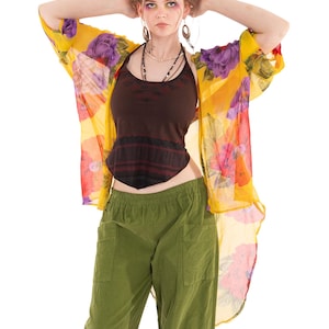 May include: A woman's outfit comprising a yellow floral print kimono, a brown halter top, and olive green cargo trousers. The kimono features purple and red flowers. The outfit is accessorised with layered necklaces and earrings.