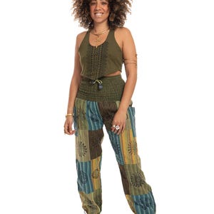 May include: An olive green sleeveless crop top with a black geometric pattern and a matching olive green high-waisted smocked waistband pant featuring a patchwork design of blue, green, and yellow stripes with black sun and circular motifs.