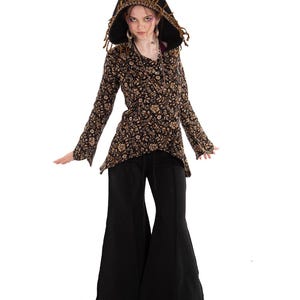 May include: A long-sleeved hooded tunic featuring a black and tan floral pattern with fringe trim along the hood edge, paired with solid black wide-leg trousers that flare at the bottom. The tunic has a pointed hemline and long sleeves.