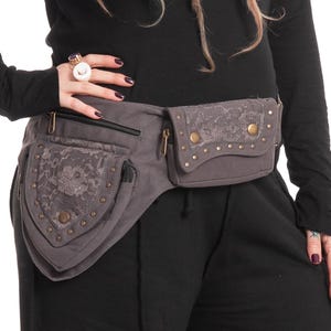 Può includere: Marsupio grigio con più tasche con cerniera e dettagli decorativi in pizzo. Il marsupio presenta borchie e cerniere color ottone. Il design è un mix di funzionalità e stile, adatto per trasportare l'essenziale.
