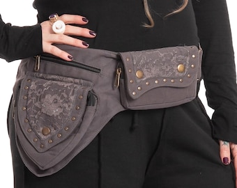 May include: Gray fanny pack with multiple zippered pockets and decorative lace accents. The pack features brass-colored studs and zippers. The design is a blend of functionality and style, suitable for carrying essentials.