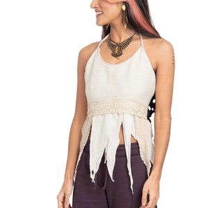 May include: A woman wearing a white halter top with a crocheted trim and purple trousers. She is wearing a brown and gold necklace with a large stone pendant.