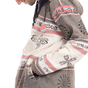 May include: A hooded jacket with a striped pattern in shades of gray, pink, and blue. The jacket has a zipper closure and a drawstring hood. The fabric is printed with black floral designs and a symbol with two eyes.