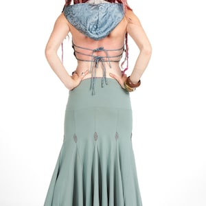 Puede incluir: Vista trasera de una mujer con un top con capucha azul claro y una falda larga verde salvia. El top tiene una espalda con cordones y la falda presenta costuras decorativas. La mujer tiene rastas rosas.