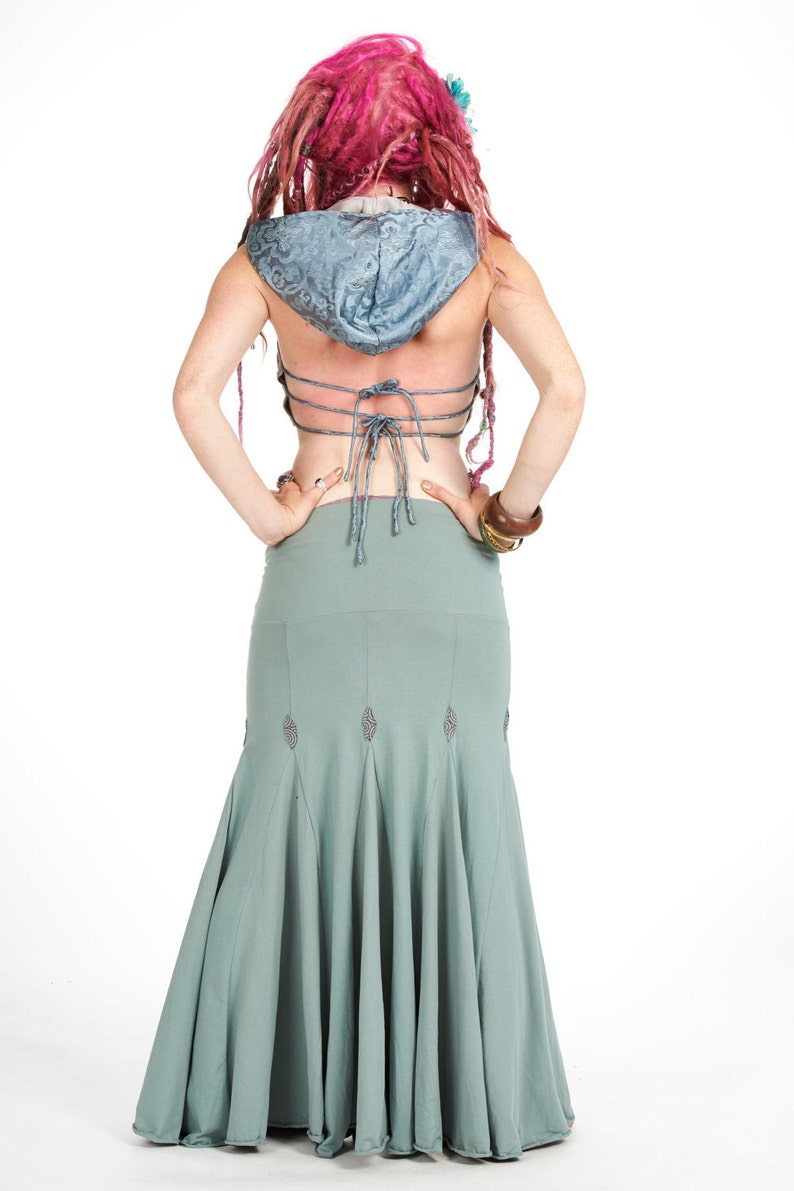 Puede incluir: Vista trasera de una mujer con un top con capucha azul claro y una falda larga verde salvia. El top tiene una espalda con cordones y la falda presenta costuras decorativas. La mujer tiene rastas rosas.