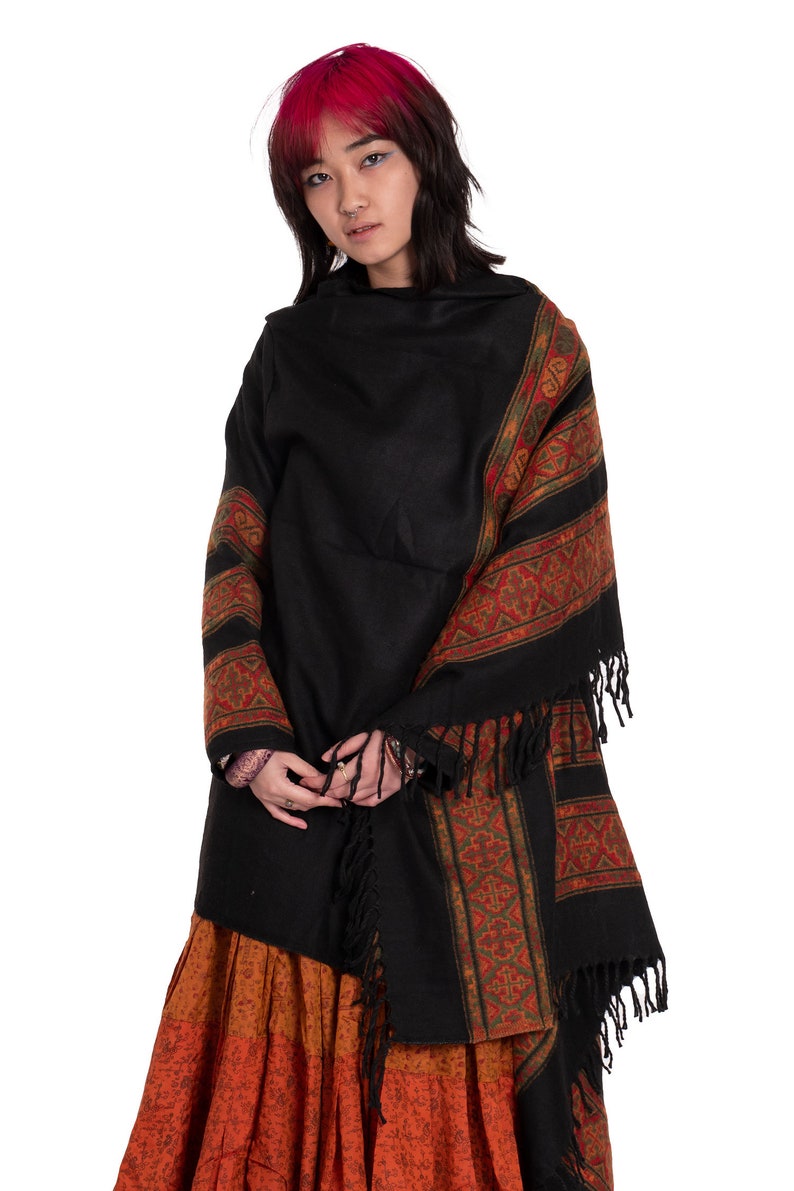 May include: A black shawl with a colorful geometric pattern and fringe trim. The shawl is draped over a person wearing a long orange skirt.