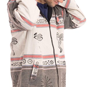 May include: A white and gray striped hooded jacket with black and white eye and sun designs. The jacket has a zipper closure and a pocket on the left side.