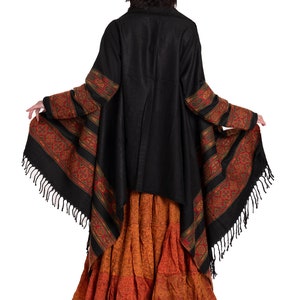 May include: A black shawl with a colorful patterned border and fringe. The shawl is worn over a long, orange and brown skirt.