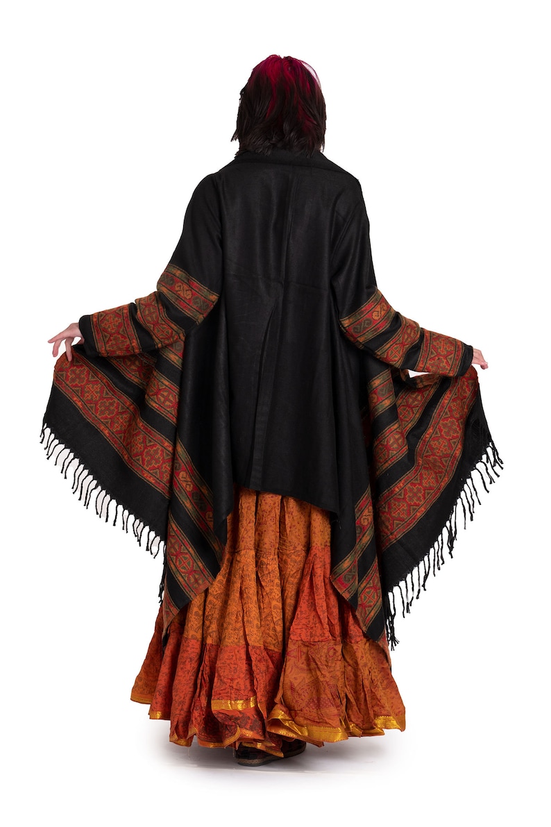 May include: A black shawl with a colorful patterned border and fringe. The shawl is worn over a long, orange and brown skirt.