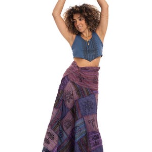 Peut inclure: Un haut court bleu sans manches avec un motif géométrique sombre sur le devant et une longue jupe portefeuille fluide présentant un design en patchwork dans des tons de violet et de bleu avec des motifs noirs imprimés de soleils, d'arbres et de fleurs.