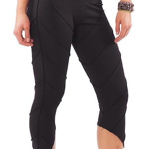 Può includere: Leggings neri a pinocchietto con una serie di cuciture diagonali in rilievo che creano un motivo a chevron lungo le gambe. Il capo presenta una silhouette aderente e termina a metà polpaccio con un orlo asimmetrico e appuntito.