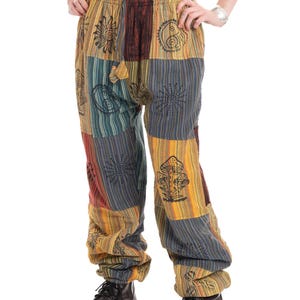 Può includere: Pantaloni patchwork multicolore con ricami di soli, funghi e simboli yin-yang. I pantaloni combinano pannelli gialli, blu e rossi. Hanno un elastico in vita e sono indossati con stivali neri. Misurano circa 100 cm di lunghezza.