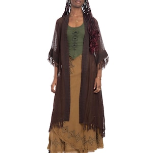 May include: A woman in a layered outfit. The ensemble features a dark brown open cardigan with fringe, a green top, and a long tan skirt with a geometric pattern. Black boots complete the look. The outfit has a bohemian style.