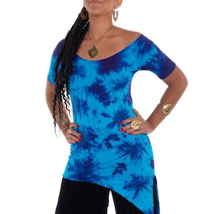 May include: A short-sleeved, off-the-shoulder tunic featuring a vibrant tie-dye pattern in shades of bright blue and deep navy. The garment has a fitted silhouette and an asymmetrical hemline that is longer on one side, paired with black trousers.