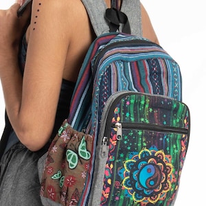 Może przedstawiać: Wielokolorowy plecak z szarym panelem tylnym z płótna. Przód plecaka zdobi duży, kolorowy wzór mandali z symbolem yin yang w środku. Plecak ma również mniejszą kieszeń z wzorem motyla.