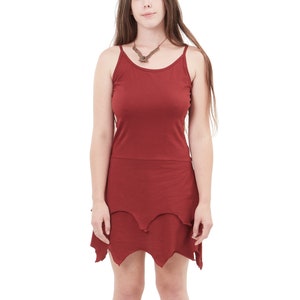 Puede incluir: Una mujer con un vestido de tirantes color burdeos con un dobladillo festoneado. Lleva un collar marrón con un colgante.