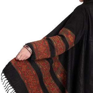 May include: Black shawl with a geometric pattern in shades of red, orange, and green. The shawl has a fringe border and is made of a soft, warm fabric.
