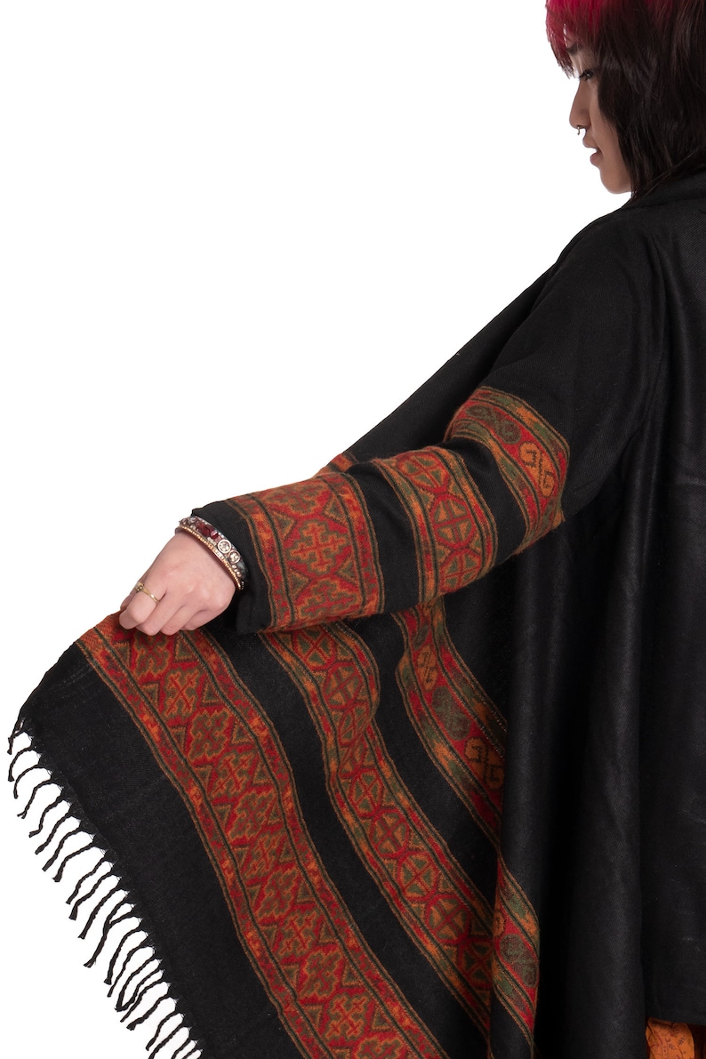 May include: Black shawl with a geometric pattern in shades of red, orange, and green. The shawl has a fringe border and is made of a soft, warm fabric.