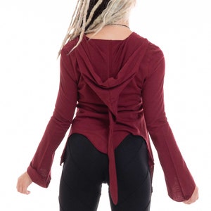 Può includere: Un top con cappuccio a maniche lunghe color bordeaux con un lungo laccio sul retro. Il top è realizzato in un tessuto morbido ed elastico e ha una vestibilità rilassata. La modella indossa leggings neri.