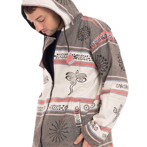 May include: A gray and white hooded jacket with a zipper closure and a patterned design featuring black and white floral motifs, a sun symbol, and a stylized eye design. The jacket has a hood with a drawstring.