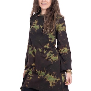 May include: A long-sleeved tunic featuring a black base color with a green tie-dye pattern. The garment has a round neckline and an asymmetrical hemline that falls longer on one side. The fabric appears to be a soft cotton jersey material.