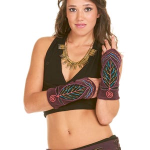 Può includere: Una donna indossa un top nero e una collana d'oro. Indossa anche un paio di guanti senza dita viola scuro con un disegno a foglia ricamato con filo colorato. I guanti hanno un disegno a spirale sul polso.