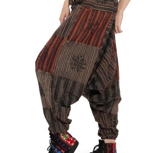 以下が含まれることがあります： 茶色のパッチワークハーレムパンツ、ウエストはドローストリング。 茶色、赤、タンの色合いのストライプと柄の生地が混ざっています。 足首は伸縮性があります。 カラフルな柄の生地を使った黒のハイカットスニーカーを履いています。