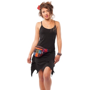 Puede incluir: Un vestido negro con un dobladillo asimétrico único. Se lleva una riñonera de patchwork colorida en la cintura. La modelo también lleva una flor roja en el pelo y una pulsera.