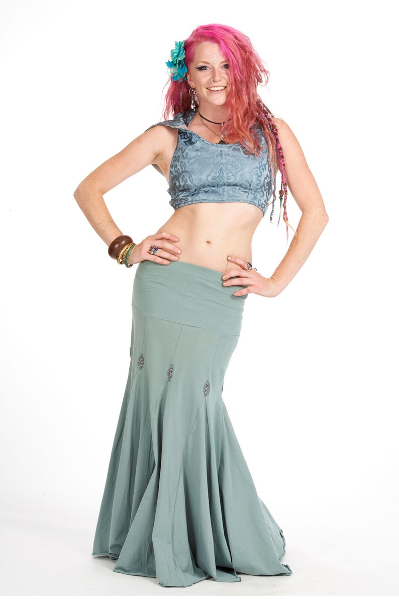Puede incluir: Un conjunto de baile de dos piezas de color turquesa. La parte superior es de estilo halter con un estampado floral. La falda es de estilo sirena fluida con detalles bordados. La modelo tiene el pelo rosa y lleva joyas.