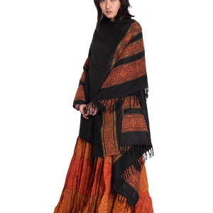 May include: A woman with pink hair wearing a black shawl with a colorful patterned border and a long orange and brown skirt.