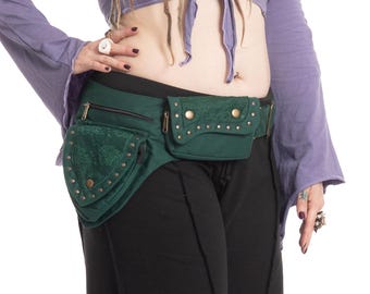 May include: A dark green hip bag with multiple pockets and gold-colored studs. The bag has a belt and is worn around the waist. The pockets have a textured appearance. The person is wearing black pants and a purple top.