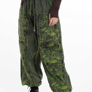 Puede incluir: Pantalón cargo verde con estampado de setas y costuras amarillas. El pantalón tiene varios bolsillos y cintura con cordón.