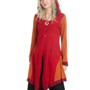 May include: A long-sleeved tunic in shades of red and orange with a hood. The tunic features a button-down front and a patterned design on the red fabric. The sleeves and side panels are a solid orange color. The model is wearing black pants.