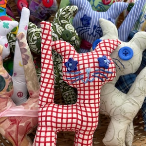 May include: A collection of stuffed fabric cat toys in various patterns and colors, including red and white gingham, floral prints, and blue plaid. Each cat features button eyes, embroidered whiskers, and stitched details, all clustered together.