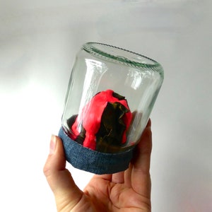May include: A glass jar with a black and red clay sculpture inside. The jar is decorated with a blue denim band around the rim.