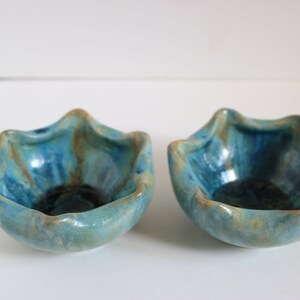 May include: Two small, blue and brown ceramic bowls with a wavy rim. The bowls are glazed in a mottled blue and brown pattern.