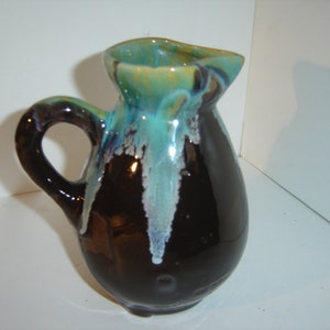 May include: A small, brown ceramic pitcher with a blue and green glaze. The pitcher has a rounded body and a handle.
