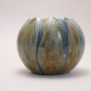 May include: A small, round ceramic vase with a blue, green, and gold glaze. The vase has a slightly ruffled top.