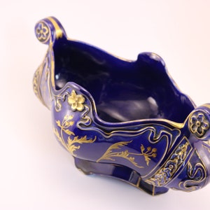 Puede incluir: Un cuenco de cer&aacute;mica azul cobalto con dise&ntilde;os florales y de volutas doradas. El cuenco tiene forma de barco y tiene dos asas.